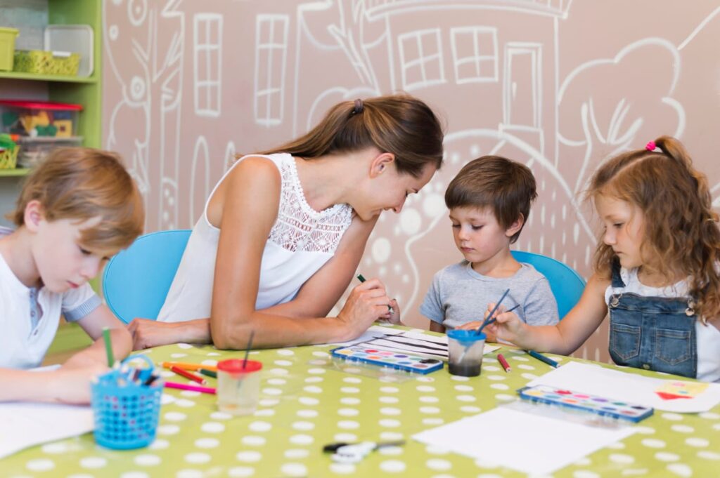 Une professeure et 3 enfants de maternelle travaillent sur une table et des chaises.